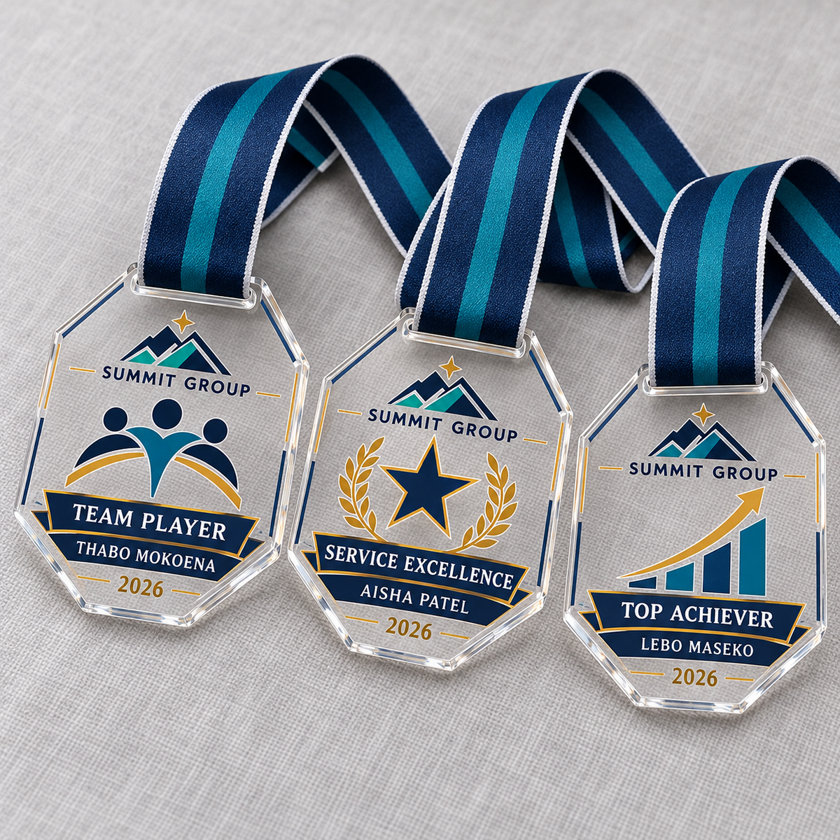 Clear acrylic corporate recognition medals with personalised DTF designs and navy and teal ribbons